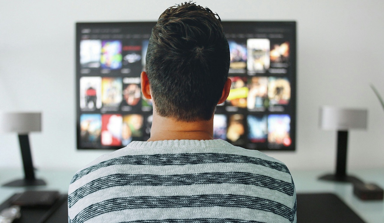 Mężczyzna siedzi przed dużym telewizorem i wybiera film z platformy internetowej.
